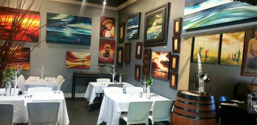 a restaurant with white tables and chairs and paintings on the walls at 44 on Ennis Guest Lodge and Restaurant - NO LOAD SHEDDDING in Ermelo