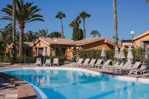 una piscina con sillas, sombrillas y palmeras en Maspalomas Resort by Dunas en Maspalomas