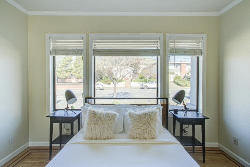1 dormitorio con 1 cama blanca, 2 mesitas de noche y 2 ventanas en South SF 3br w balcony backyard near shops SFO-1655, en South San Francisco