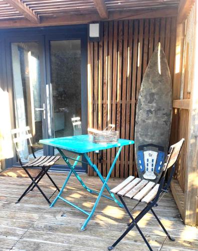 una mesa y dos sillas y una tabla de surf en un porche en La petite cabane de Georges à Saint Brévin l'Océan, en Saint-Brevin-les-Pins