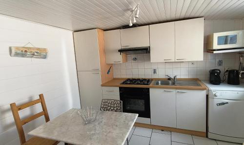 une cuisine avec des armoires blanches, une table et un micro-ondes dans l'établissement La petite maison bleue 2 à 3 personnes, à Andernos-les-Bains