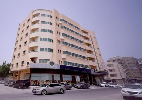 AL MARJAN FURNISHED APARTMENTS في عجمان: مبنى كبير به سيارات تقف في موقف للسيارات