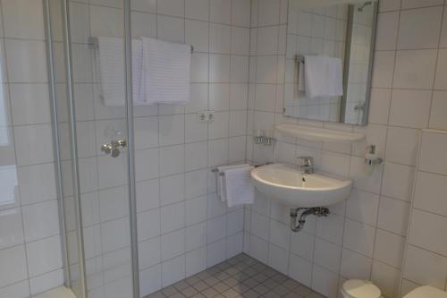 a white tiled bathroom with a sink and a shower at Landgasthof Kirschgarten in Ingelheim am Rhein