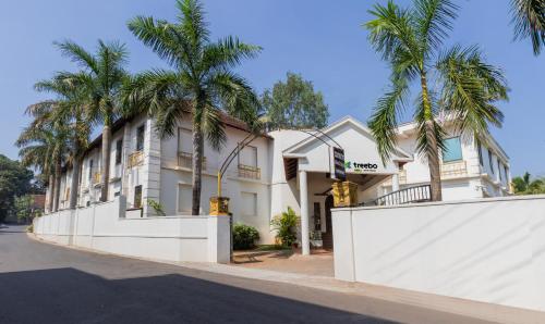 a white building with palm trees in front of it at Treebo Trend Sadhoo Heritage Ayurvedic Spa & Pool in Kannur