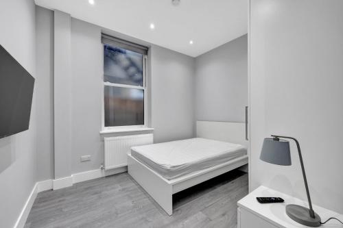 a small white room with a bed and a window at Your Cosy Stay Modern 1 Double Bedroom Flat Fully Furnished - 5 Mins walk to Stn in London