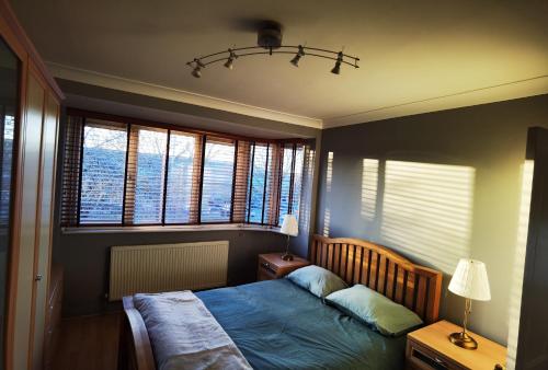 Schlafzimmer mit einem Bett mit blauer Decke und Fenstern in der Unterkunft ANAND HOUSE in Harrow