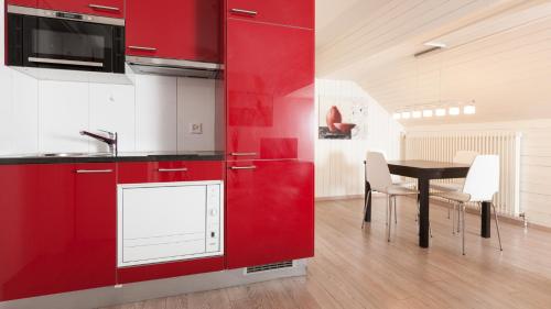 una cocina con armarios rojos y una mesa con sillas. en Swiss Star Marc Aurel - Self Check-In, en Zúrich
