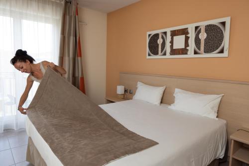 a woman standing next to a bed in a hotel room at The Originals Boutique, Hotel l'Occitan, Aubagne in La Destrousse