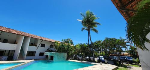 a swimming pool in front of a hotel with a palm tree at Apart Hotel Farol de Itapuã - Suíte com cozinha completa à 250m da praia e farol de Itapuã in Salvador