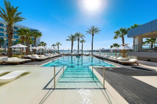 a swimming pool with lounge chairs and palm trees at Amàre Beach Hotel Ibiza - Adults Recommended in San Antonio Bay