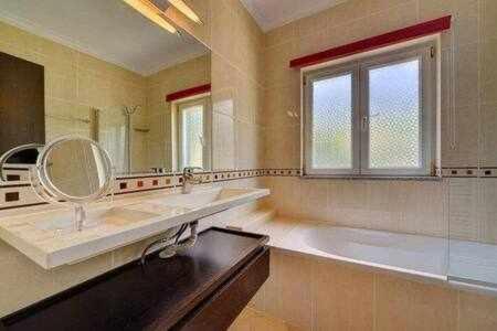 ein Badezimmer mit einer Badewanne, einem Waschbecken und einem Spiegel in der Unterkunft Villa 3 quartos piscina a 3km Vilamoura in Boliqueime
