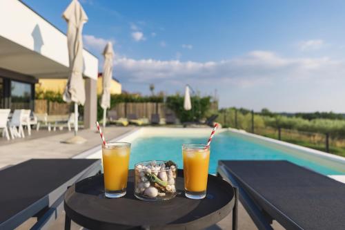 deux verres de jus d'orange sur une table à côté d'une piscine dans l'établissement Villa Boiky - private pool and amazing sea view, Istria, à Materada