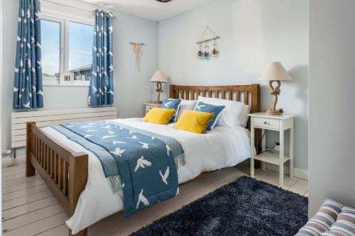 una camera da letto con letto, lenzuola bianche e blu e cuscini gialli di Wooda Farm Holidays a Bude