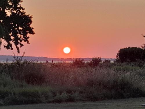 a sunset in a field with the sun in the sky at Bright summer house close to the beach and water in Holbæk