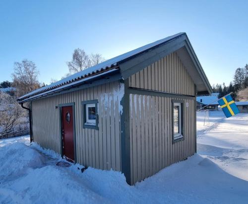 un petit bâtiment avec une porte rouge dans la neige dans l'établissement Sjöställe Gudö, annexet, à Vendelsö