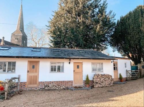 une maison blanche avec des portes en bois et une église dans l'établissement Priory Cottage Stables, à Cowden