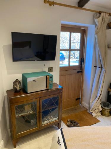 a living room with a tv on the wall and a table at Priory Cottage Stables in Cowden