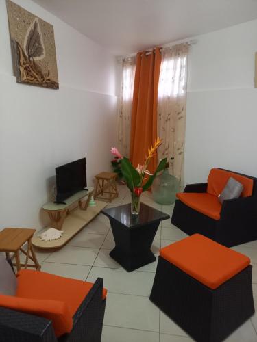 a living room with orange and black furniture and a tv at Location Les Arômes Anse Mitan Trois Ilets Martinique in Les Trois-Îlets
