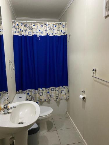 a bathroom with a sink and a toilet and a blue shower curtain at Arriendo casa por día in Villarrica