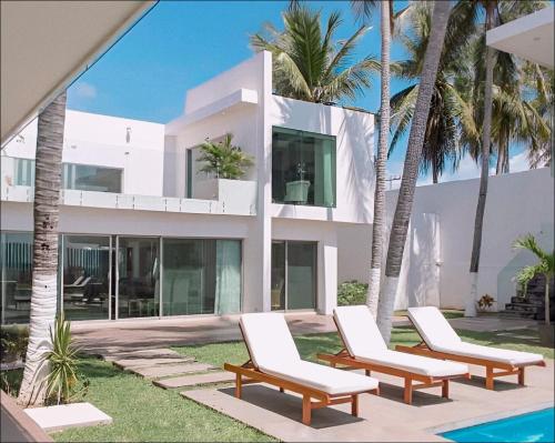 a white house with two lounge chairs and palm trees at Luxury Palms Puerto Arista in Puerto Arista