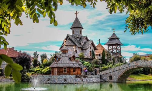 a church in the middle of a lake with a bridge at Etno selo Stanišići Hotel Pirg in Dvorovi