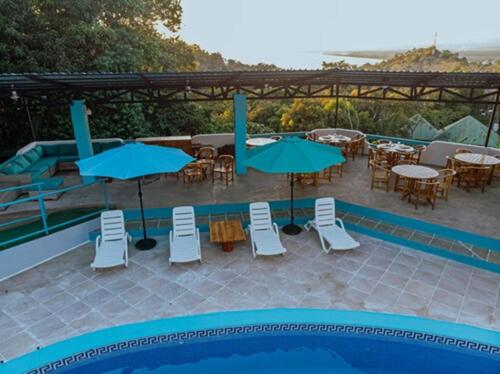 a pool with tables and chairs and blue umbrellas at Hotel Planeta Sano in Manuel Antonio