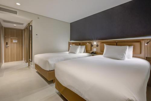 two beds in a hotel room with white sheets at Hilton Garden Inn São José do Rio Preto in Sao Jose do Rio Preto