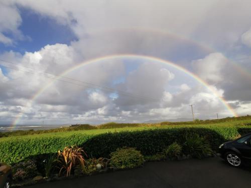 a rainbow in the sky over a field with a car at Ocean Heights B&B in Lissadell