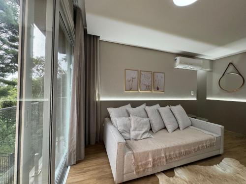 um sofá branco num quarto com uma grande janela em Alpes da Montanha 404 - Apê Novo em Gramado em Gramado