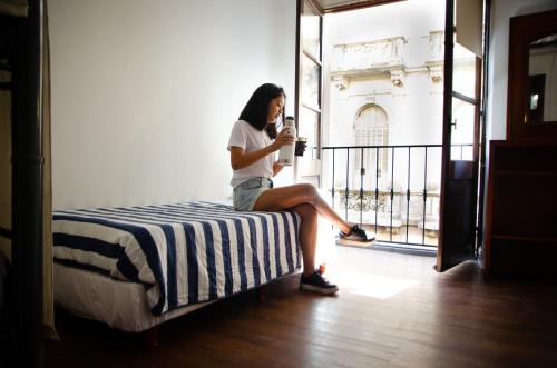 a woman sitting on a bed looking at her cell phone at BA Stop Hotel House in Buenos Aires