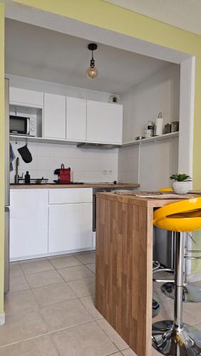 cocina con armarios blancos y taburete amarillo en Bel appartement F3 tout confort, en Saint-Vincent-de-Paul