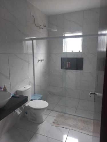 a white bathroom with a shower and a toilet at Casa com piscina em condomínio fechado in Peruíbe