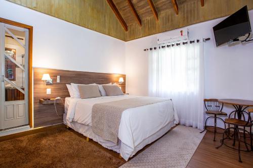 a bedroom with a bed and a table and a television at Pousada Suiça Mineira Garden in Monte Verde