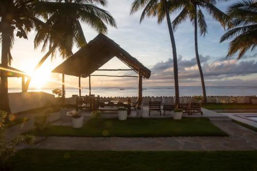 a patio with a gazebo with palm trees and the sunset at Oasys House - Beautiful Private Beach Front Home in Msambweni