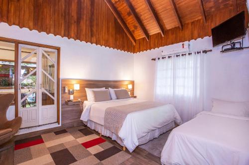 a bedroom with two beds and a tv and a window at Pousada Suiça Mineira Garden in Monte Verde