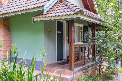 a small green house with a wooden porch at Pousada Suiça Mineira Garden in Monte Verde
