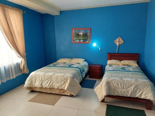 a blue bedroom with two beds and a window at Hostal y Complejo Turístico La Rueda in Guaranda