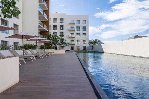 a swimming pool with chairs and umbrellas next to a building at Lumina at Marea Cabo San Lucas in Cabo San Lucas