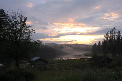 a sunset over a lake with a house and trees at Rustika strandstugor utanför Rättvik in Rättvik
