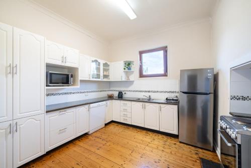 a kitchen with white cabinets and a stainless steel refrigerator at MèRose Place - Cottage on George in Bathurst