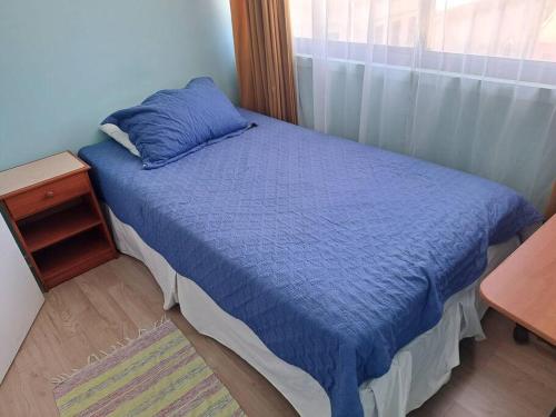 a bedroom with a bed with a blue blanket and a window at Departamento en cerro placeres in Valparaíso