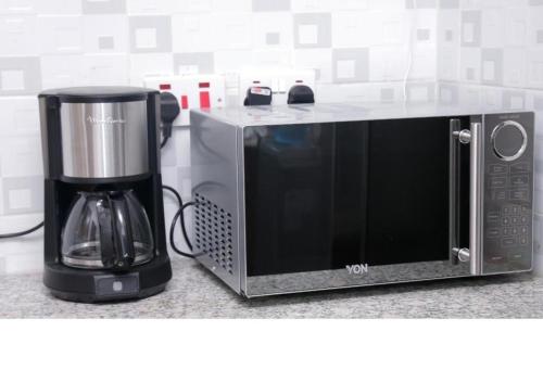 - un four micro-ondes assis sur un comptoir à côté d'une cafetière dans l'établissement 3 BEDROOM LIWANDO HOME at Greatwall Gardens next to Greatwall Mall, 15 Minutes from JKIA Airport With FREE WIFI & Parking, Enjoy Entire Unit in a Gated Community manned with Security 24 Hours, à Athi River