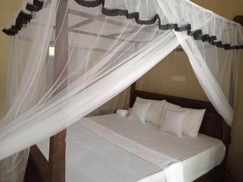 1 dormitorio con cama con dosel y cortinas blancas en Appu Villa, en Tangalle