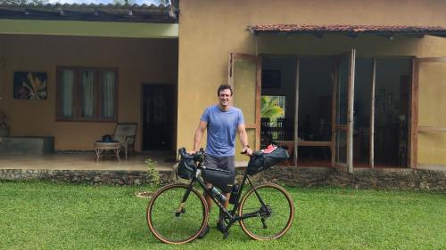 Ein Mann steht neben einem Fahrrad vor einem Haus. in der Unterkunft Rivendell Twisted Tree in Kurunegala