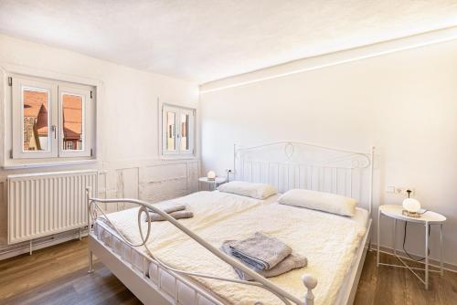 a white bedroom with a bed and two windows at Ferienwohnungen Metzgerpost in Altensteig