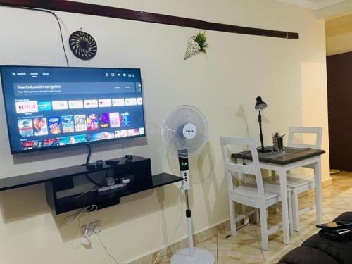 Habitación con TV y mesa con ventilador. en Muggiez Olive, Kira, en Kampala