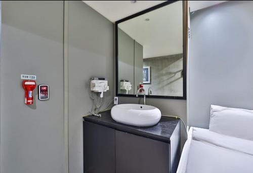 a bathroom with a sink and a mirror next to a bed at MVG Motel in Geoje 