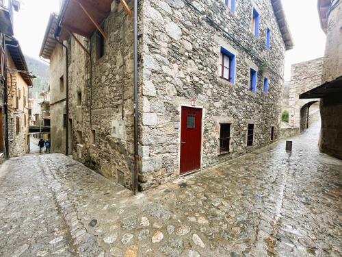 a stone building with a red door on a street at Apartamento dúplex en el puente histórico, Gra de Fajol in Camprodon