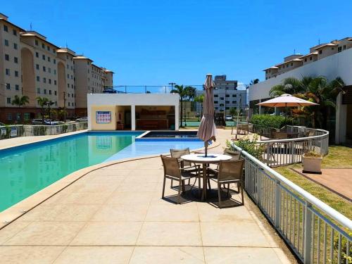 d'une terrasse avec une table et des chaises à côté de la piscine. dans l'établissement Apartamento aconchegante em condomínio perto da praia, à Ilhéus