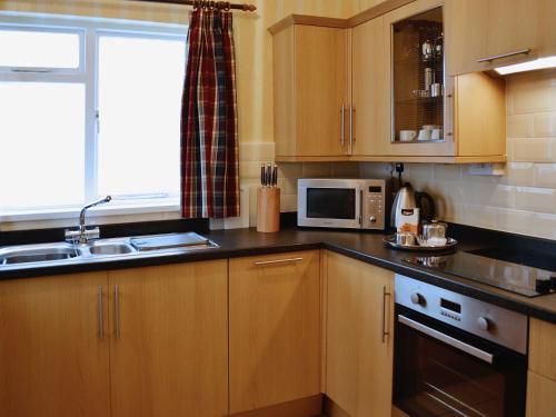 a kitchen with wooden cabinets and a sink and a microwave at Nelson - Fdg in Ilfracombe